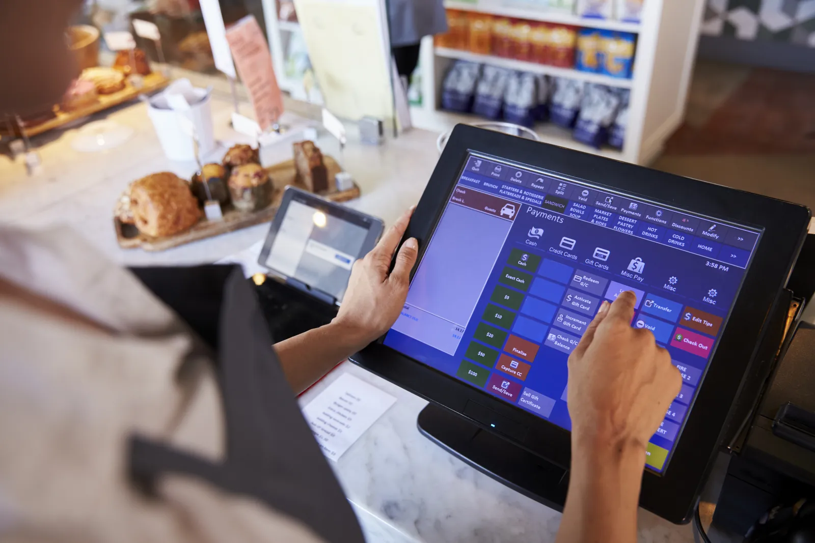 A member of staff taking a payment on an EPOS touchscreen in a cafe.